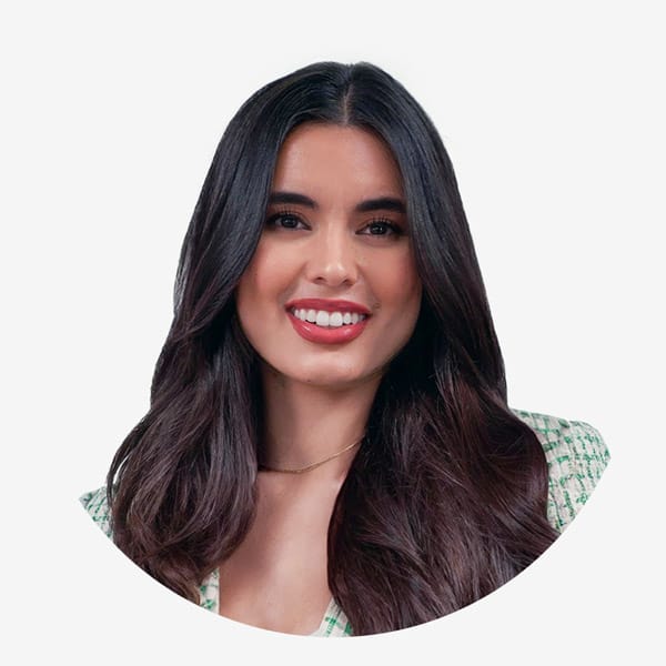 A woman with long dark hair and a light green patterned top smiles at the camera against a plain white background, holding her Service Dog Registration certificate.