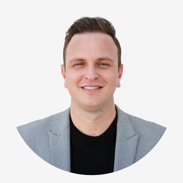 A man with short brown hair wearing a light gray blazer over a black shirt smiles at the camera against a plain white background, representing confidence often seen in Service Dog Certifications professionals.