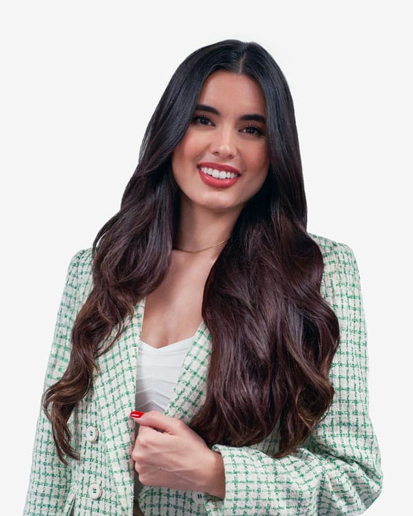 Woman with long dark hair wearing a light green plaid blazer and white top, smiling and facing the camera against a plain white background.